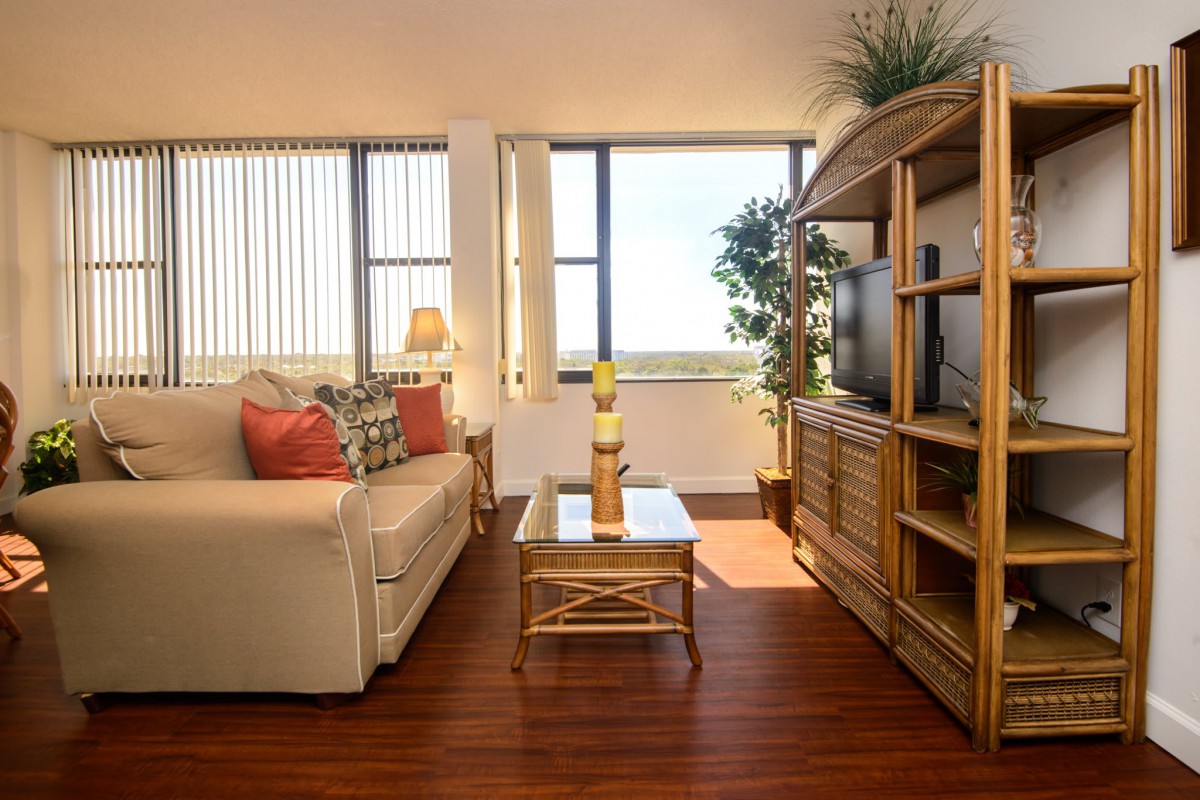 A cozy living room with wooden furniture, a sofa, and a television, bathed in natural sunlight.