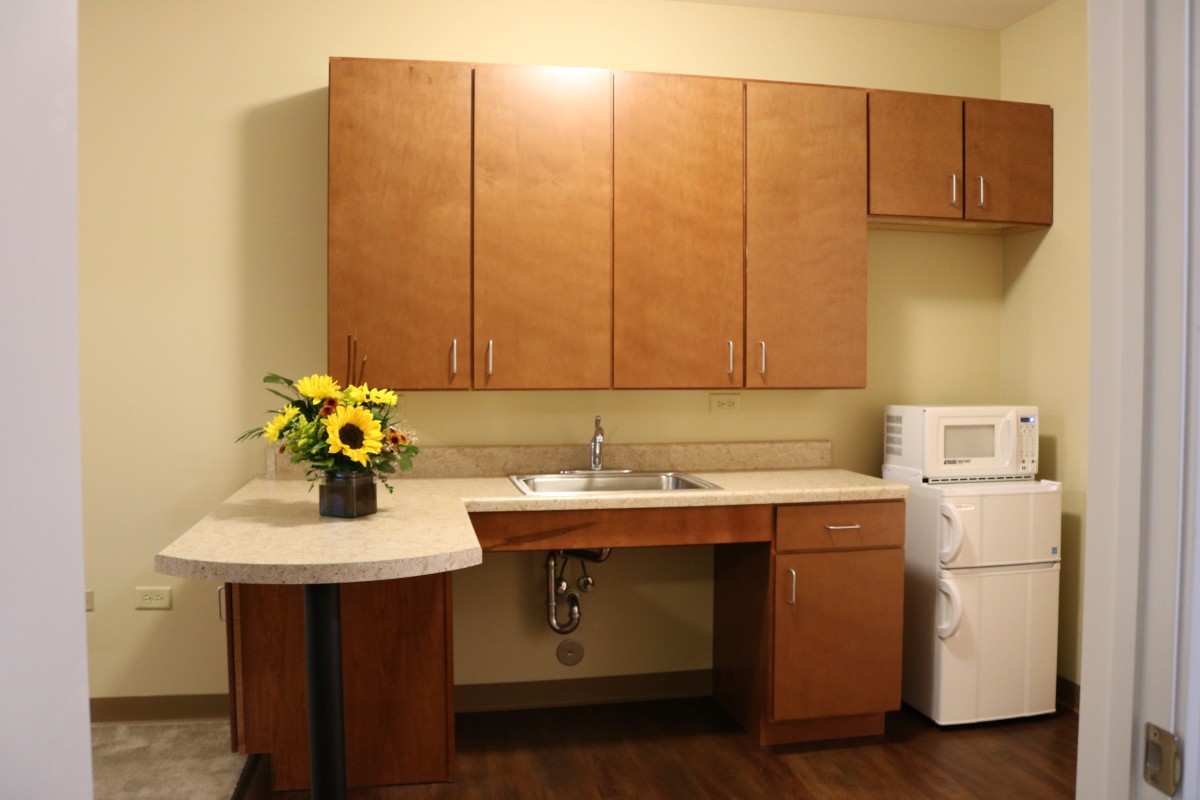 A kitchen area with wooden cabinets, a sink, and a vase of sunflowers on the countertop. A washer is also visible.