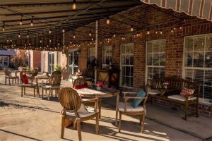 A cozy outdoor patio with wooden furniture and string lights under a sunny sky.