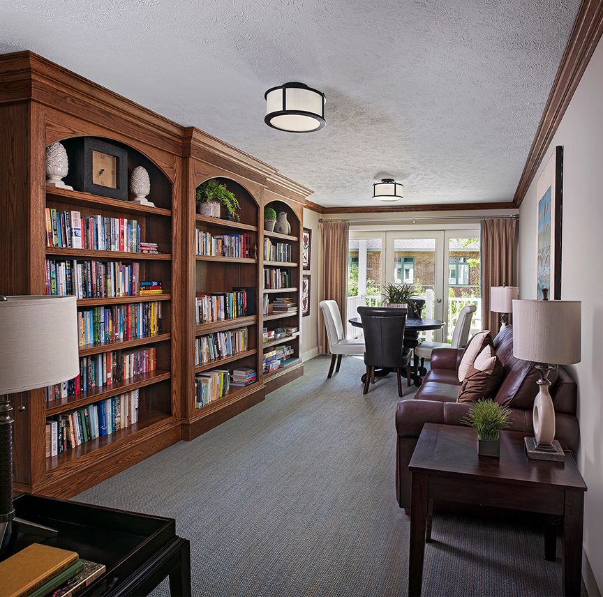 A cozy library room with wooden bookshelves, armchairs, and a conference table.