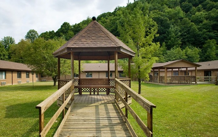 A wooden gazebo with a walkway surrounded by lush greenery and trees.