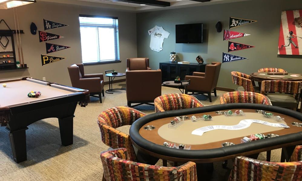 A stylish game room featuring a poker table, pool table, and cozy seating area with sports decorations on the walls.
