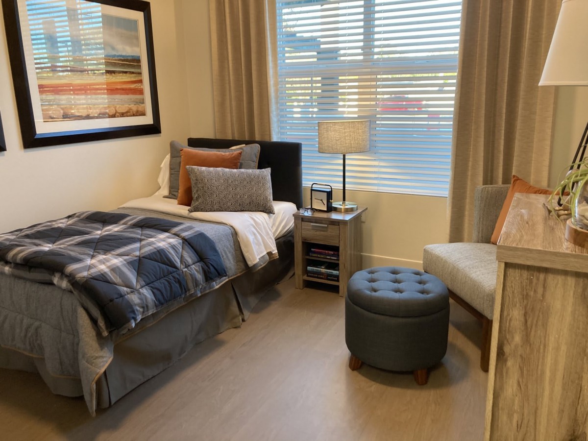 A cozy bedroom with modern decor featuring a bed, lamp, chair, and window.