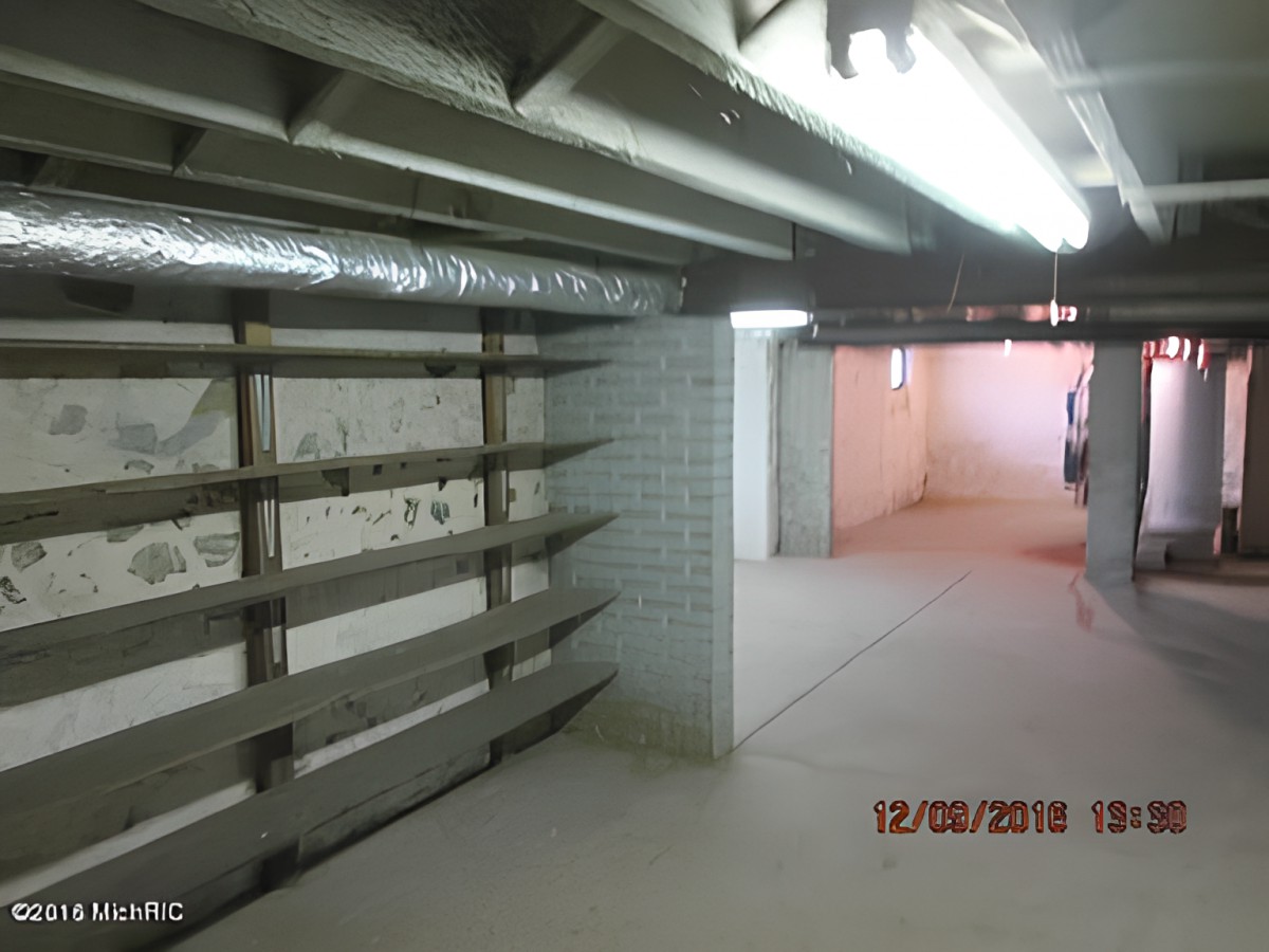 An empty basement with exposed ceiling beams and concrete flooring.