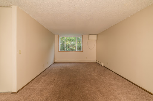 An empty room featuring neutral-colored walls and carpet, with a window allowing natural light.