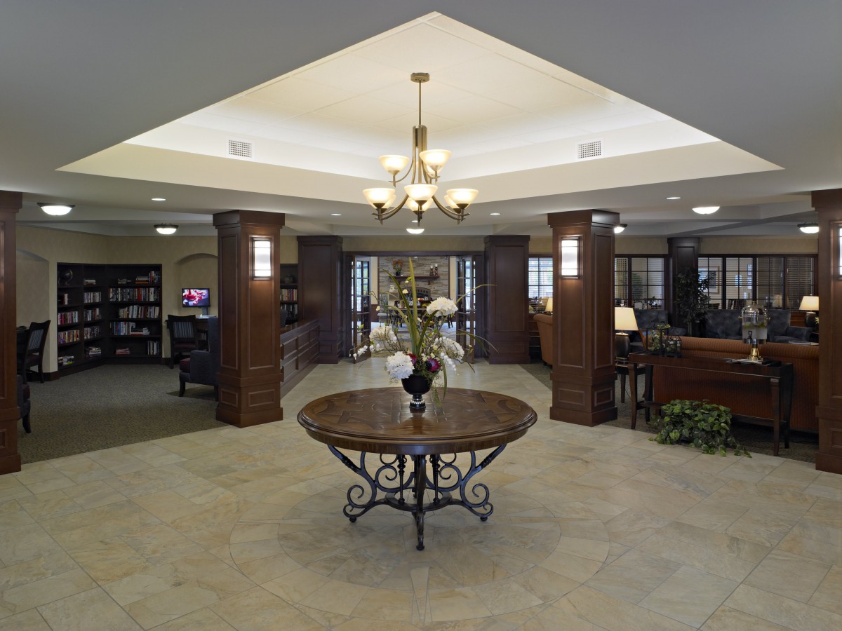A spacious lobby area featuring a chandelier, circular table with floral arrangement, and decorative columns.