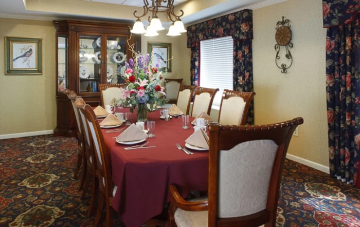 An elegant dining room set with a red tablecloth and floral centerpiece, surrounded by wooden chairs.