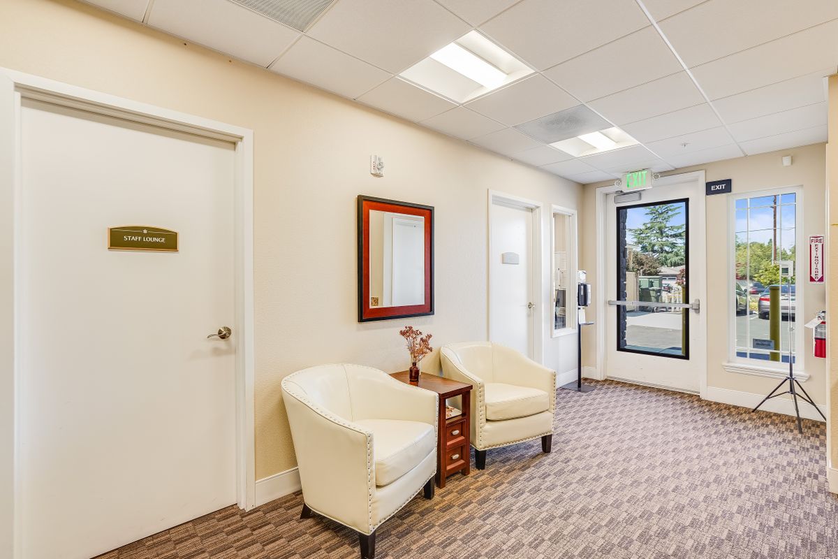 A cozy waiting room featuring two white chairs, a mirror, and soft lighting.