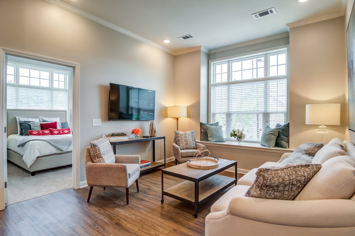 A cozy and modern living room with stylish furniture, a mounted TV, and large windows allowing natural light.