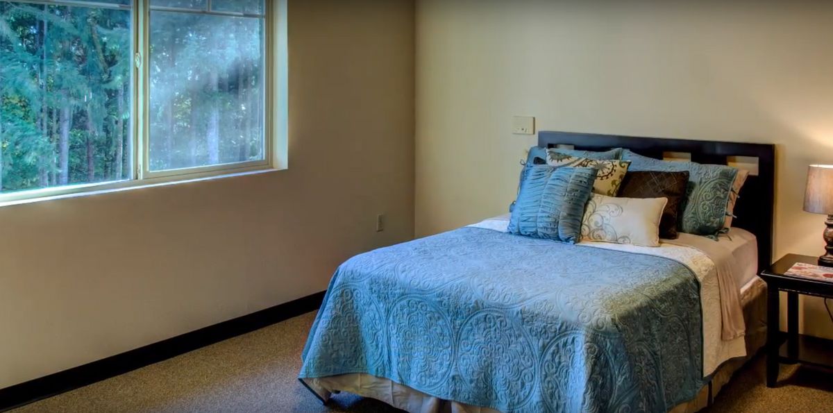 A cozy bedroom with a single bed adorned with blue bedding and a window on the side.
