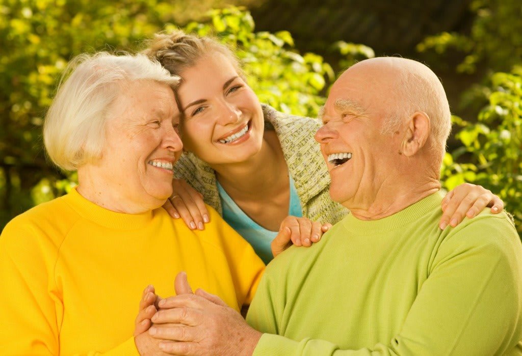A cheerful family moment outdoors, with elderly individuals and a younger woman sharing smiles and laughter.