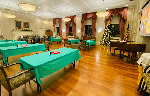 A cozy dining room set up for a festive gathering, featuring green tablecloths and a Christmas tree.