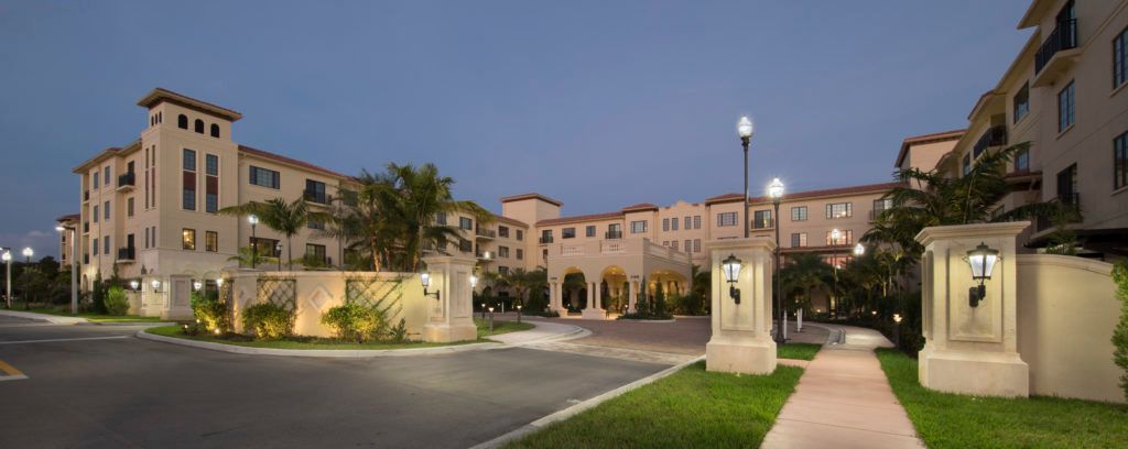 A well-lit hotel building at night with palm trees and landscaped grounds.