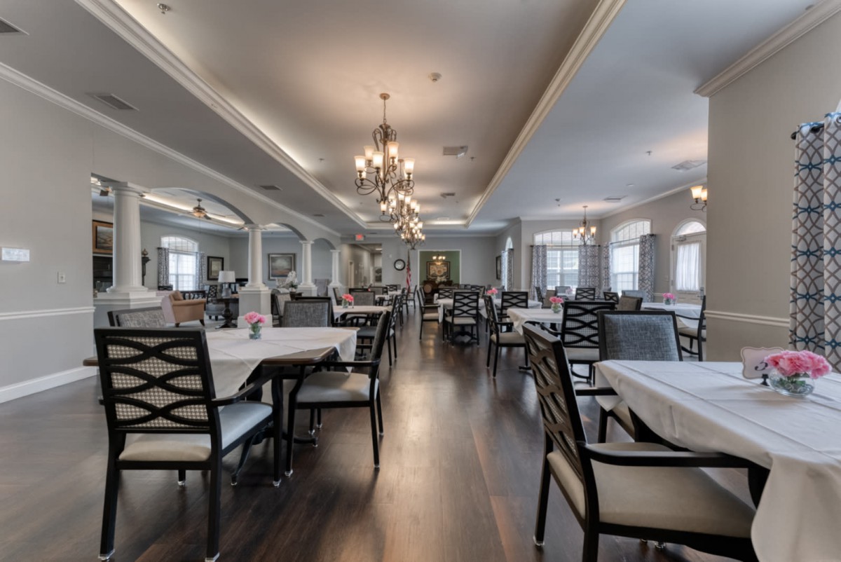 An elegant dining area with neatly arranged tables, chairs, and chandeliers under warm, bright lighting.