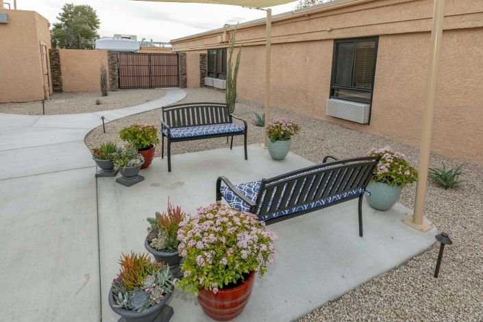An outdoor patio area with benches and potted plants, surrounded by a garden courtyard.
