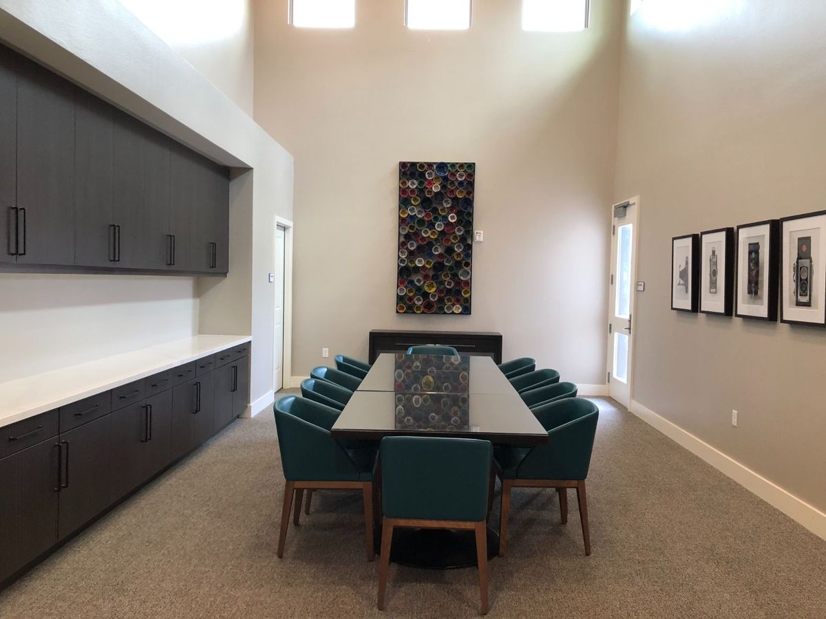 A modern dining room with a long table, surrounded by teal chairs, high ceilings, and contemporary artwork on the walls.