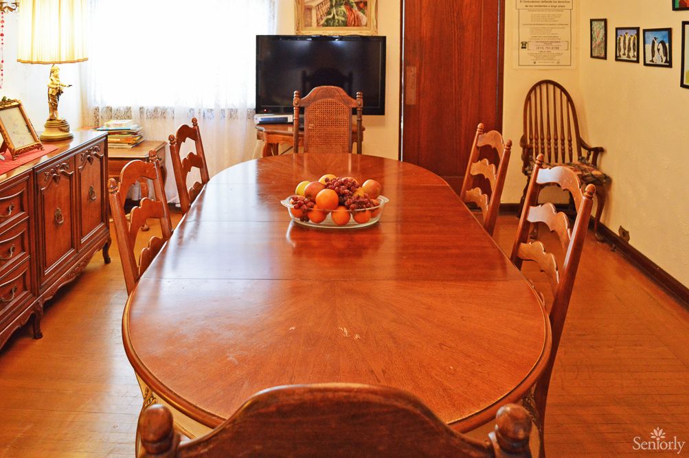 A cozy dining room featuring a wooden table with chairs and a fruit bowl centerpiece.