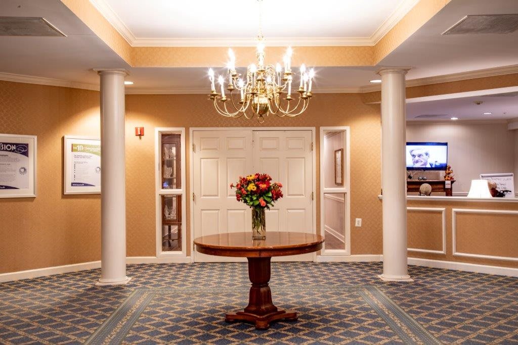 A spacious lobby with elegant decor, featuring a central table adorned with flowers and a chandelier above.