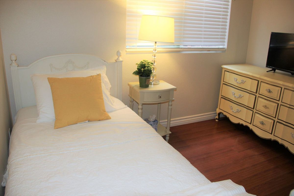 A cozy bedroom with a white bed, yellow pillow, and soft lighting from a lamp on the nightstand.