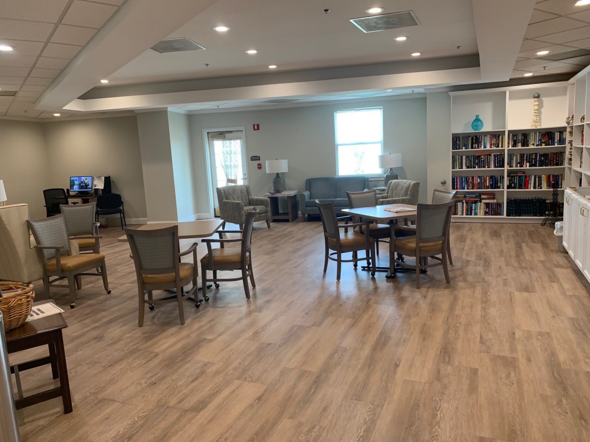 A spacious room with tables and chairs, featuring a bookshelf and wooden flooring.