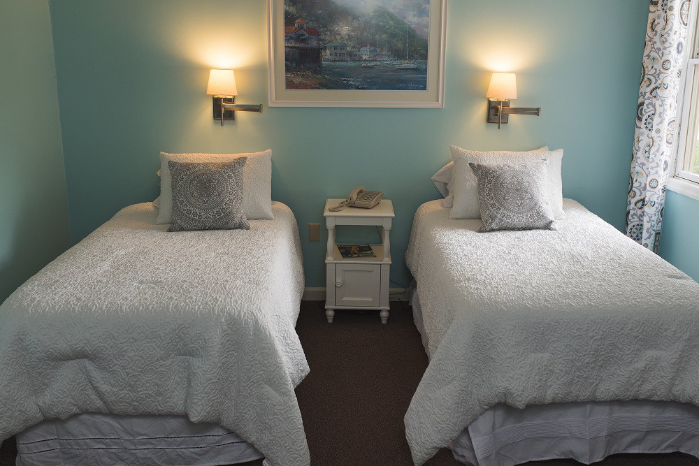 A cozy bedroom featuring two twin beds with white bedding and a central nightstand, illuminated by wall lamps.