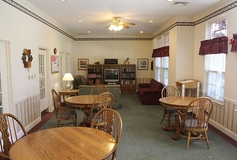 A cozy living room with multiple tables, chairs, a television, and bookshelves.
