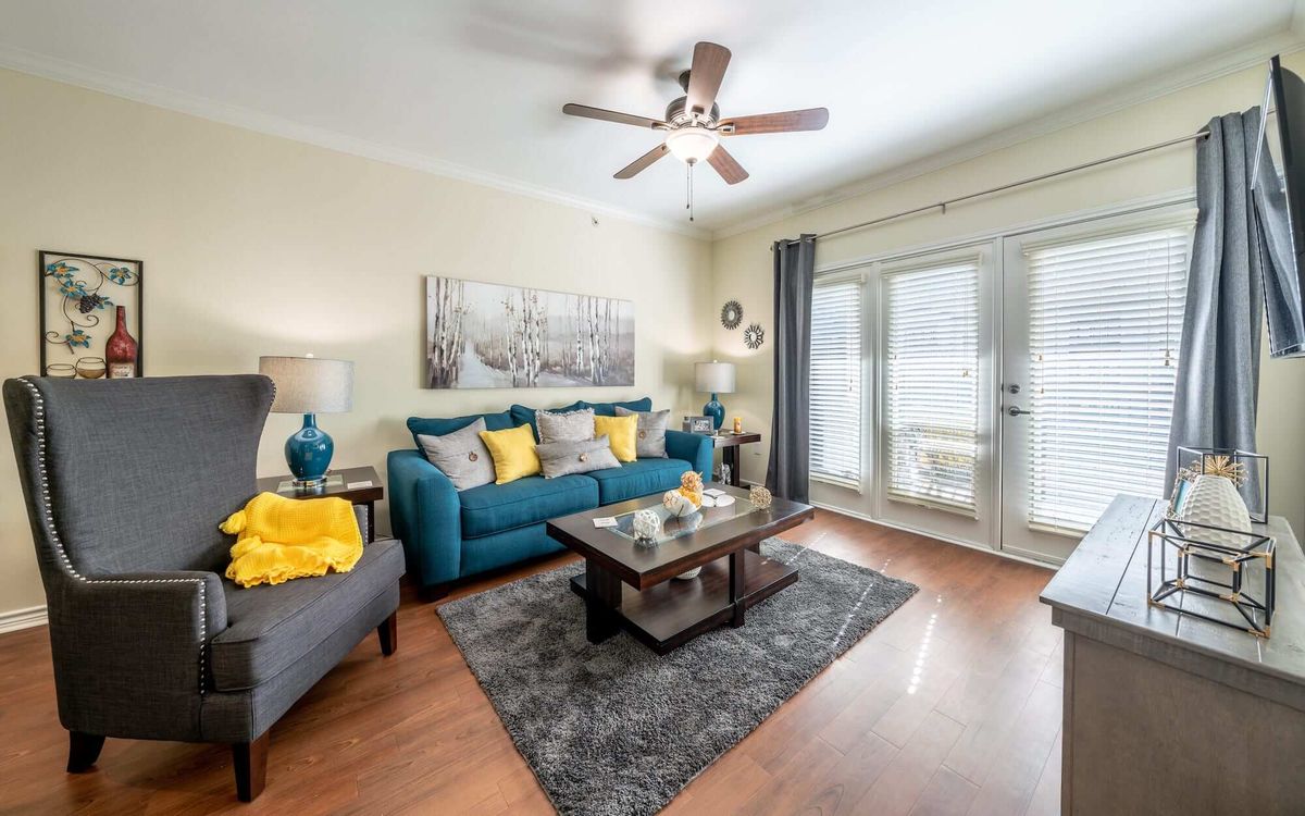 A cozy living room with teal and yellow accents, featuring a comfortable sofa, coffee table, rug, and ceiling fan.