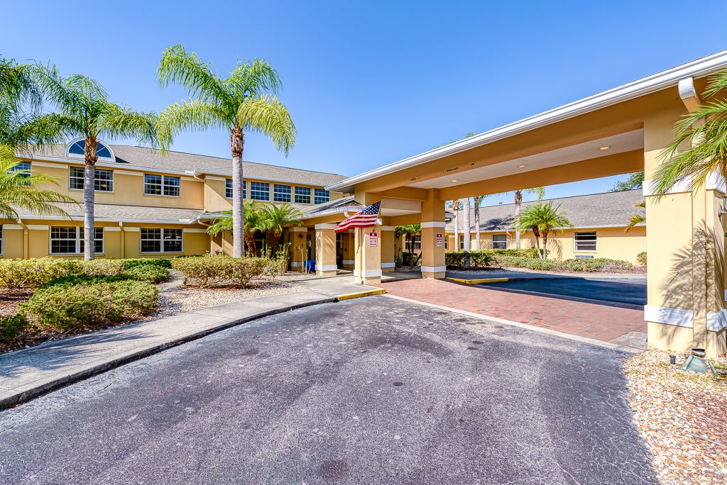 The image shows the exterior of a hotel with a covered entrance and surrounding palm trees.