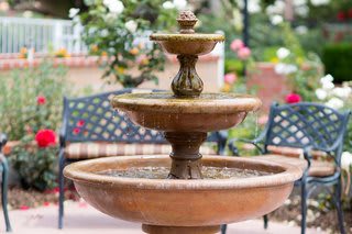 A tiered garden fountain with a bench in the background.