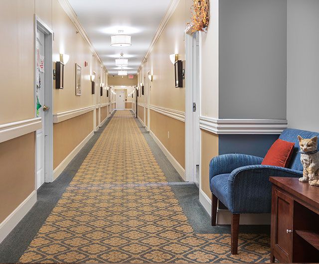 A spacious, well-lit hallway with patterned carpet and a blue chair on the side.