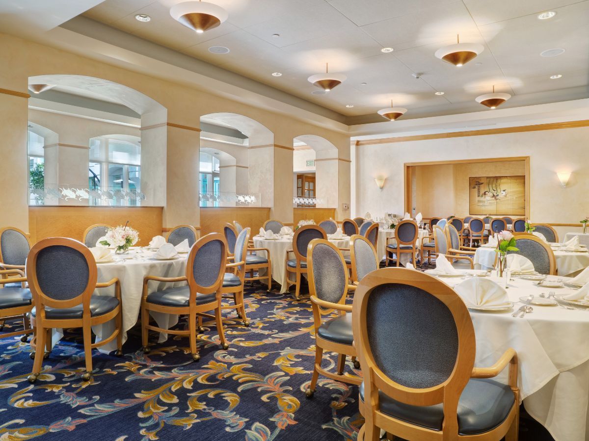 An elegant dining room with round tables and upholstered chairs, set for an event.