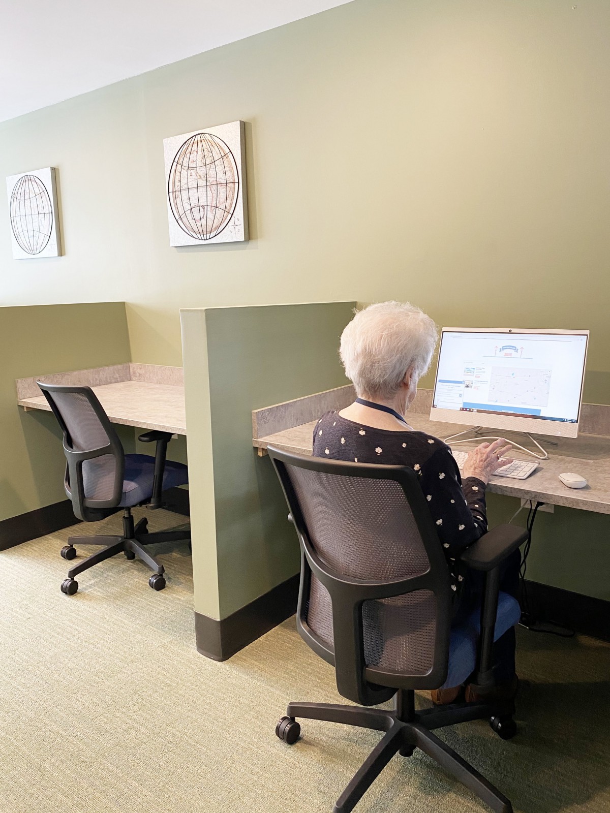 An elderly person using a computer at a shared workspace.