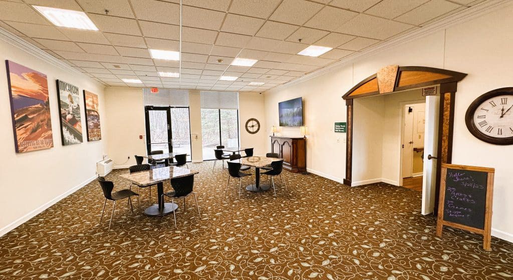 A spacious waiting area with tables, chairs, and a television in a carpeted room.