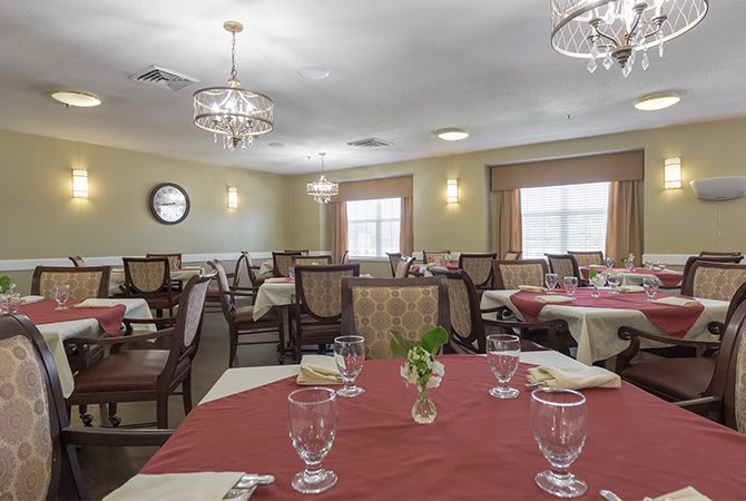 An elegant dining room with several tables and chairs, featuring chandeliers and neatly arranged place settings.