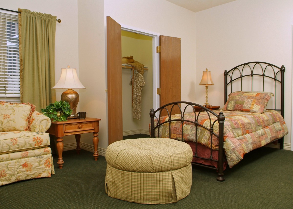 A cozy bedroom featuring a metal-framed bed, a lamp on a side table, an armchair, and a small ottoman.