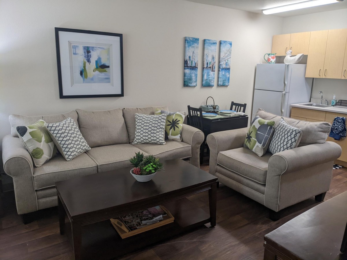 A cozy living room with a sofa, armchair, coffee table, and kitchen area.