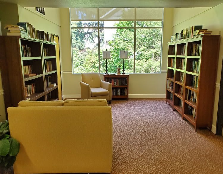 A cozy reading area with bookshelves, armchairs, and a large window overlooking greenery.
