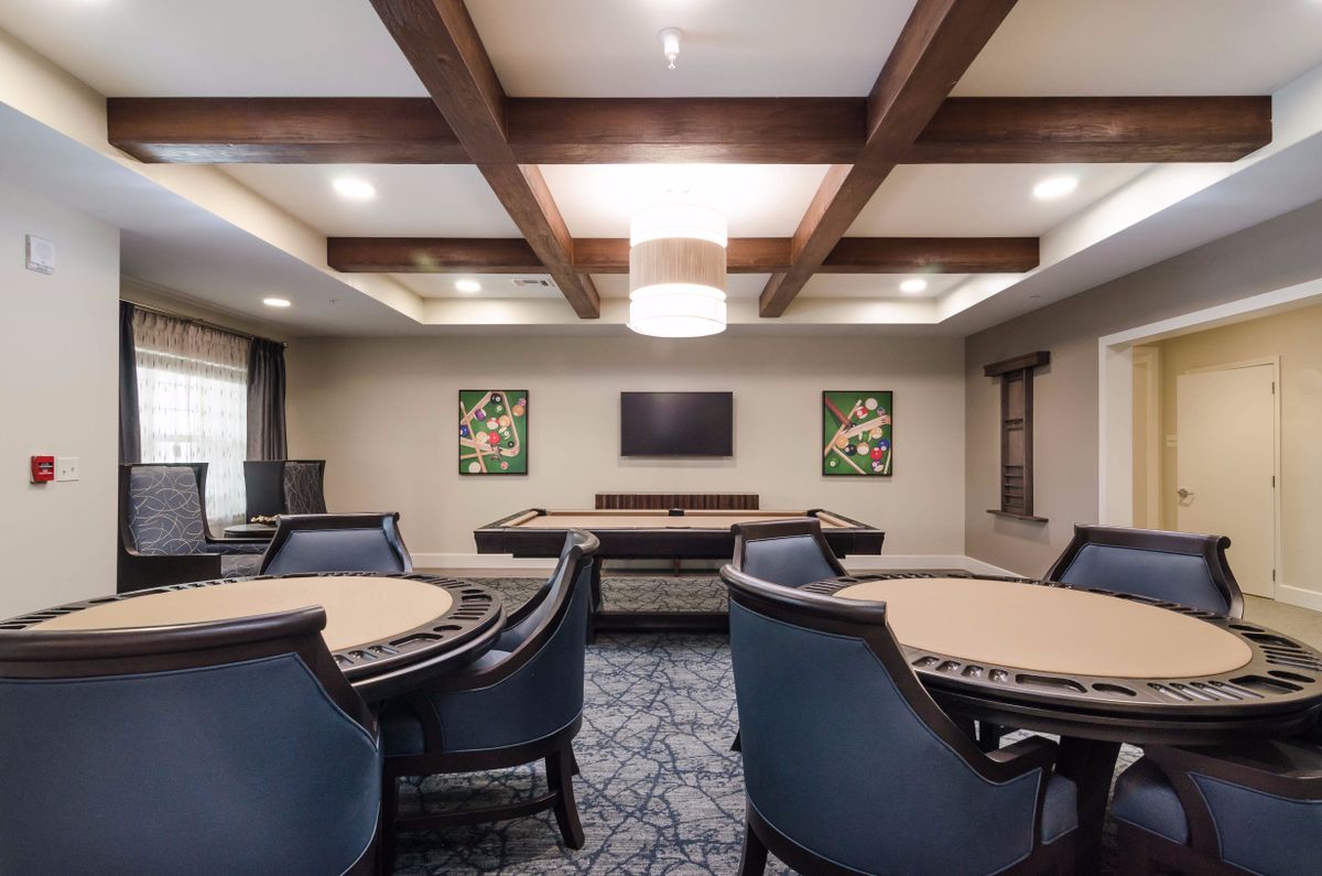 A stylish game room with poker tables and lounge chairs, featuring a mounted television and decorative artwork.