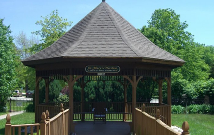 A wooden gazebo in a park surrounded by trees.