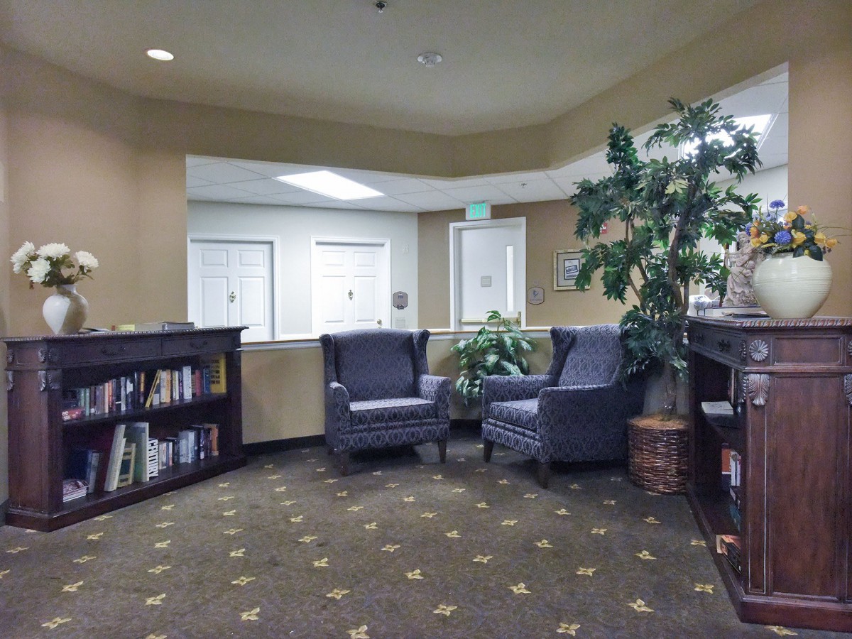 A cozy lobby featuring two armchairs, a bookshelf, and decorative plants.