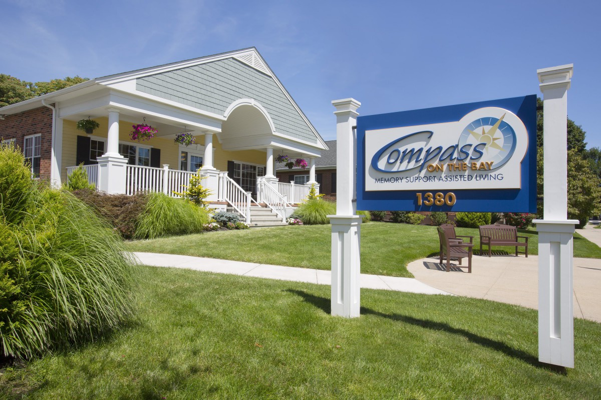 A view of the Compass Insurance office with a sign and well-maintained lawn on a sunny day.