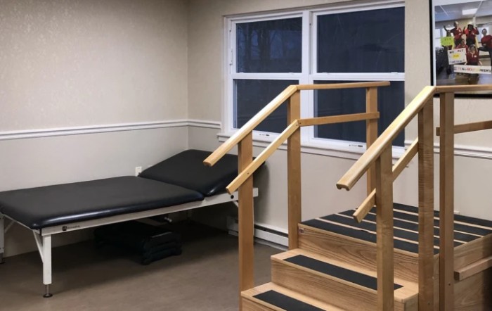 A physical therapy room featuring a set of wooden stairs and a treatment bed.