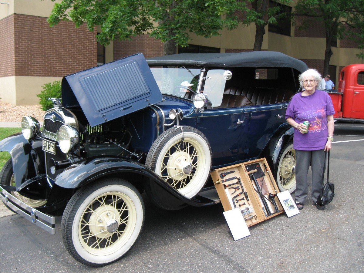 A vintage car on display outdoors with a person standing beside it.