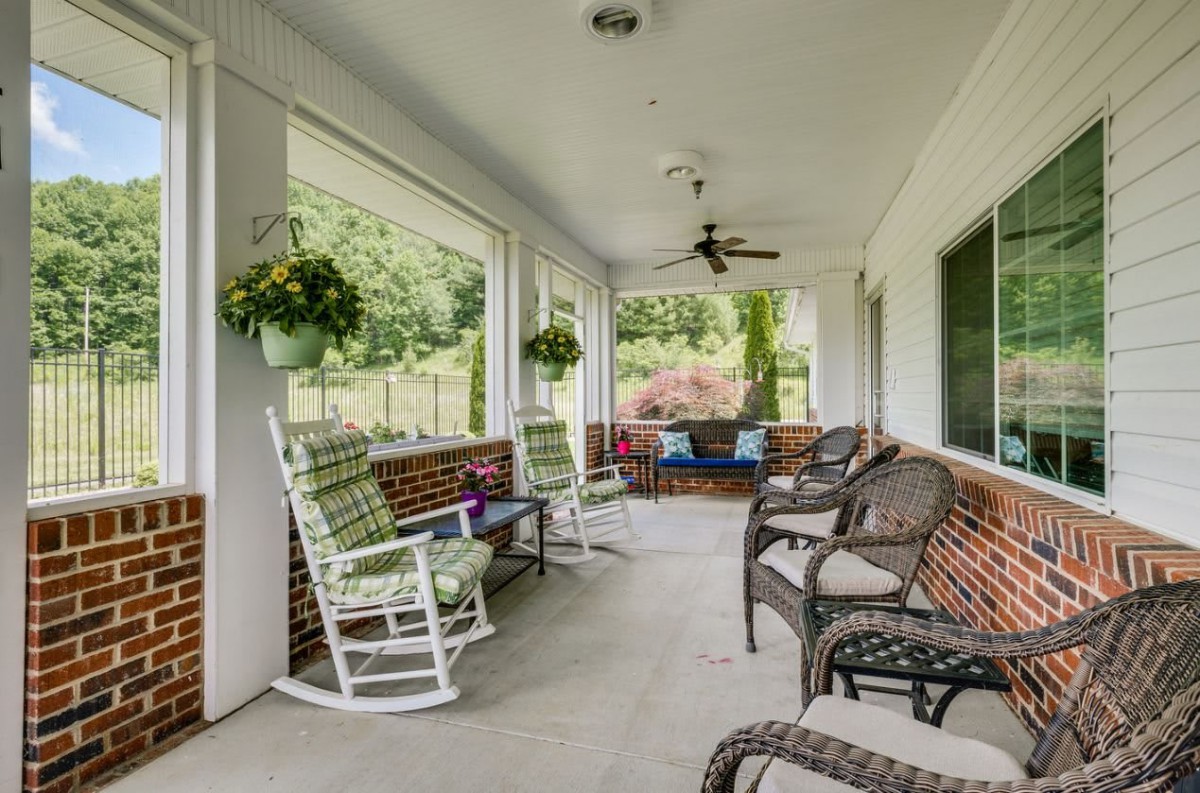 A cozy porch with rocking and wicker chairs, surrounded by greenery.
