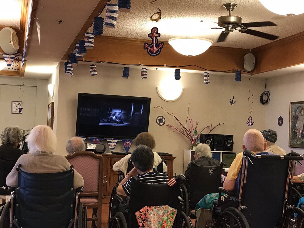 A group of elderly individuals watching television together in a nursing home.
