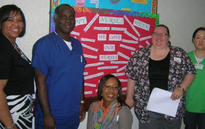 A group of three people standing and sitting in front of a bulletin board.