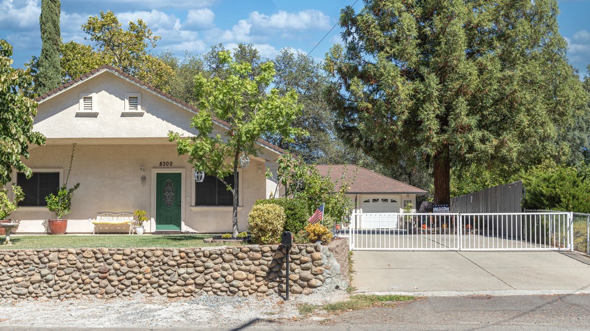 A suburban house with a stone wall, trees, and a driveway leading to a garage.