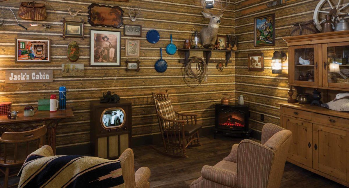 A cozy vintage living room with rustic decor, featuring an antique television, a deer mount, and a rocking chair by the fireplace.