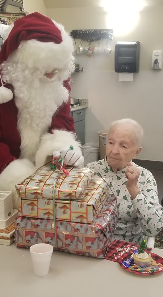 An elderly person receives gifts from Santa Claus during a Christmas celebration.
