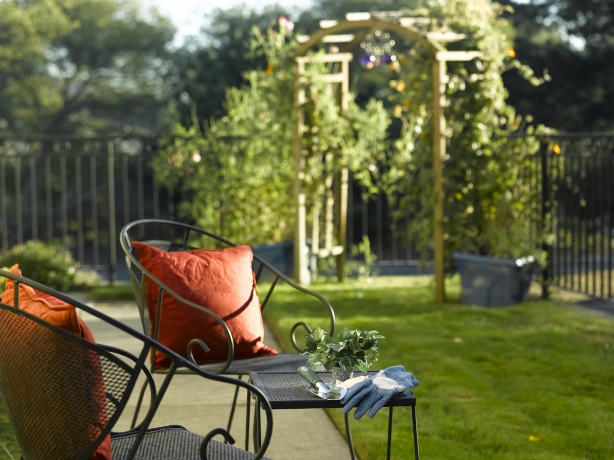A tranquil garden setup with a cozy chair and a view of an archway surrounded by lush greenery.